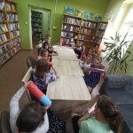 zajęcia edukacyjne w bibliotece, dzieci przy stole ćwiczą z papierowymi tubami