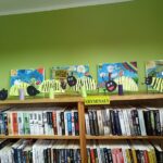 Biblioteka zajęcia edukacyjno-czytelnicze półki z ksiażkami na nich stoją prace dzieci: motyle i obrazy