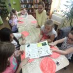 Biblioteka zajęcia edukacyjno-czytelnicze dzieci siedzą przy stole, czytają i malują