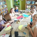 Biblioteka zajęcia edukacyjno-czytelnicze dzieci siedzą przy stole, czytająi malują