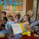 Spotkanie w przedszkolu dzieci i bibliotekarka przy stole czytają książkę