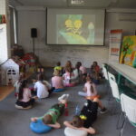 grupa dzieci siedzi na dywanie i ogląda bajkę na projektorze pt" Pszczółka Maja"