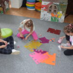 dziewczynki siedzą na dywanie i wycinają kolorowe kwiaty