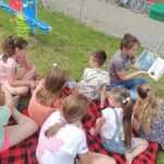 zajecia edukacyjno-czytelnicze, dzieci i słuchają bajkisiedzą na kocu na trawie