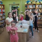zajęcia dla dzieci w filii bibliotecznej, dzieci stoją przy stole pokazują w rękach gluty