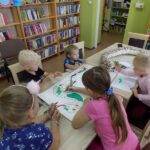 biblioteka, czytenie z maluszkami, dzieci z bibliotekarką przy stole malują węża