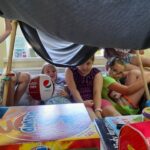 dzieci siedzą pod baldachimem z koca na kijach