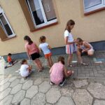 grupa dzieci maluje kolorową kredą na chodniku