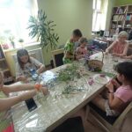 dzieci iedzą przy stole, lepią ramki z polnych kwiatów