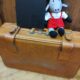 maskotka Koziołka Klemensa siedzi na walizce z dziennikiem podróży