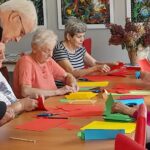 Grupa seniorów przy stole układa z origami