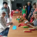 Grupa seniorów przy stole prezentuje ułożone kwiaty z origami