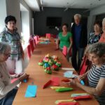 Grupa seniorów przy stole prezentuje ułożone kwiaty z origami