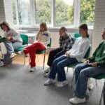 Projekt młodzieżowy, grupa młodzieży siedzi na krzesłach w okręgu, piszą