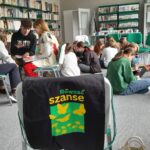 Projekt młodzieżowy, grupa młodzieży siedzi na podłodze i na krzesełkach