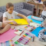 czworo dzieci siedzi przy stole i malują na kolorowych kartkach
