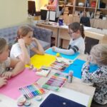 czworo dzieci siedzi przy stole i malują na kolorowych kartkach