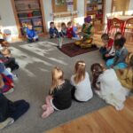 dzieci i przebrana bibliotekarka siedzą na dywanie, słuchają bajki, lampa stoi w srodku