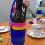 butelka ozdobiona kolorowym papierem, w tle seniorka