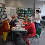 Grupa seniorów siedzi przy stołach i rozwiązują zadania