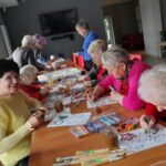 warsztaty artystyczne dla seniorów, uczestnicy pracują przy stole - kolorują liscie z papieru