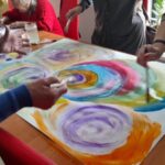 warsztaty artystyczne dla seniorów, uczestnicy pracują przy stole nak kolorowym obrazem
