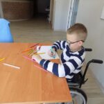 chłopiec na wózku, maluje rysunek przy stole