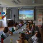 grupa dzieci ogląda film gdzie pokazane są najpiękniejsze plaże świata