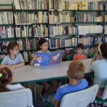 Dzieci siedzą przy stołach i czytają książkę