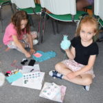 dziewczynki siedzą na dywanie i szują breloczki i lamę z materiału