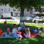dzieci siedzą na kocach na trawie i słuchają bajki