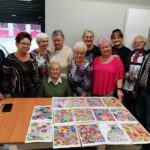 grupa seniorów - wspólne zdjęcie, kolorowe prace leża przed nimi na stole