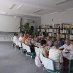 grupa seniorów siedzi przy stołach i rozwiązują zadania