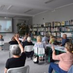 seniorzy wykonują ćwiczenia gimnastyczne na krzesełkach