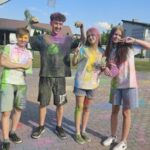 Projekt młodzieżowy Ziołowe love - cztery osoby stoją na boisku, są posypane kolorowymi proszkami holi
