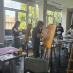 Warsztaty malarskie, młodzież maluje przy stołach i sztalugach