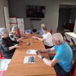 Grupa seniorów siedzi przy stole i gra w gry planszowe