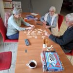 Grupa seniorów siedzi przy stole i gra w gry planszowe