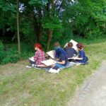 w parku, kilka młodych osób siedzi na kocu, malują