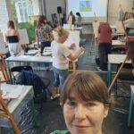 warsztaty malarskie, selfie, z tyłu reszta uczestników pracuje przy sztalugach