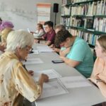 grupa uczestników warsztatów siedzi przy stole i czyta teksty