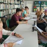 grupa uczestników warsztatów siedzi przy stole i czyta