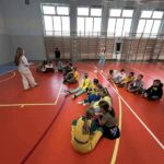na sali gimnastycznej siedzą dzieci w dwóch rzędach