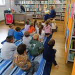 dzieci siedzą na kocyku, bibliotekarka czyta książkę