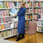 bibliotekarka stoi na tle książek, trzyma otwartą książkę