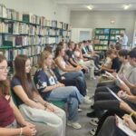 kilkanaście młodych osób siedzi na krzesłach w dwóch rzędach zwróceni twarzą do siebie