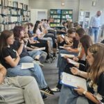 kilkanaście młodych osób siedzi na krzesłach w dwóch rzędach zwróceni twarzą do siebie
