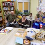 w bibliotece, uczestnicy spotkania czytają dzieciom i dorosłym siedzącym wokół