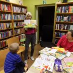 bibliotekarka pokazuje osobom siedzącym otwartą ksiażkę