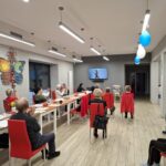 grupa osób siedzi na krzesłach i wykonuje ćwiczenia gimnastyczne